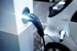 Electric charge point glowing with white light next to white car