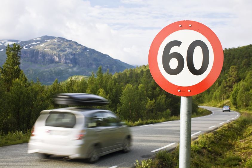 Car driving on country road past a 60mph speed limit sign