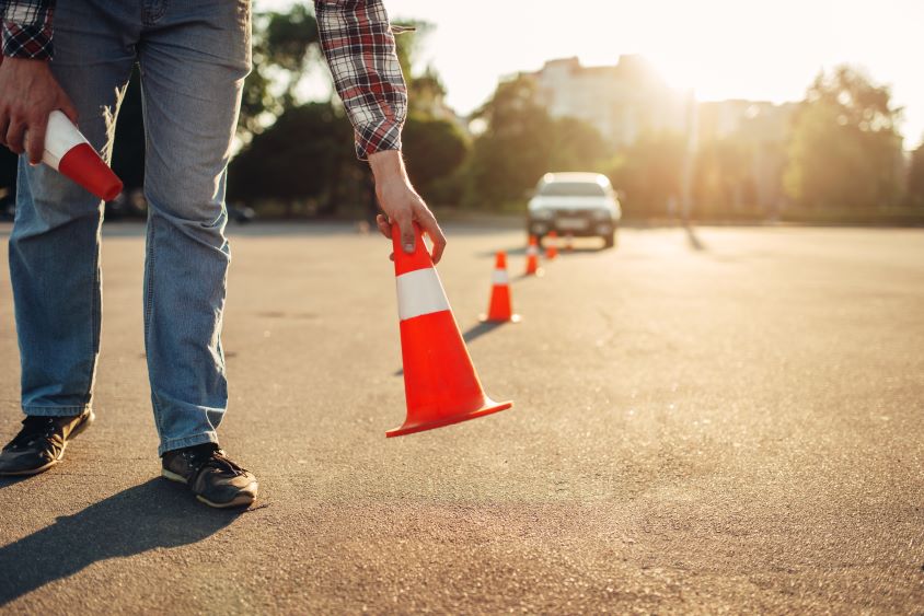 Figure laying out orange cones with car parked in background