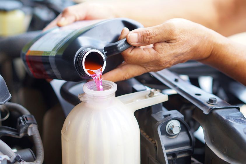 Close up of car engine, hands pouring coolant into the system