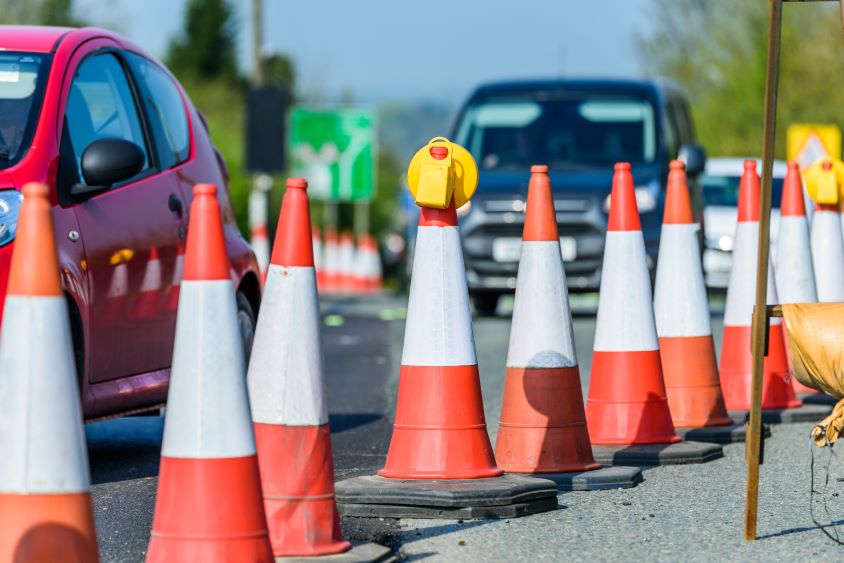 Traffic cones lined up on road, cars passing by