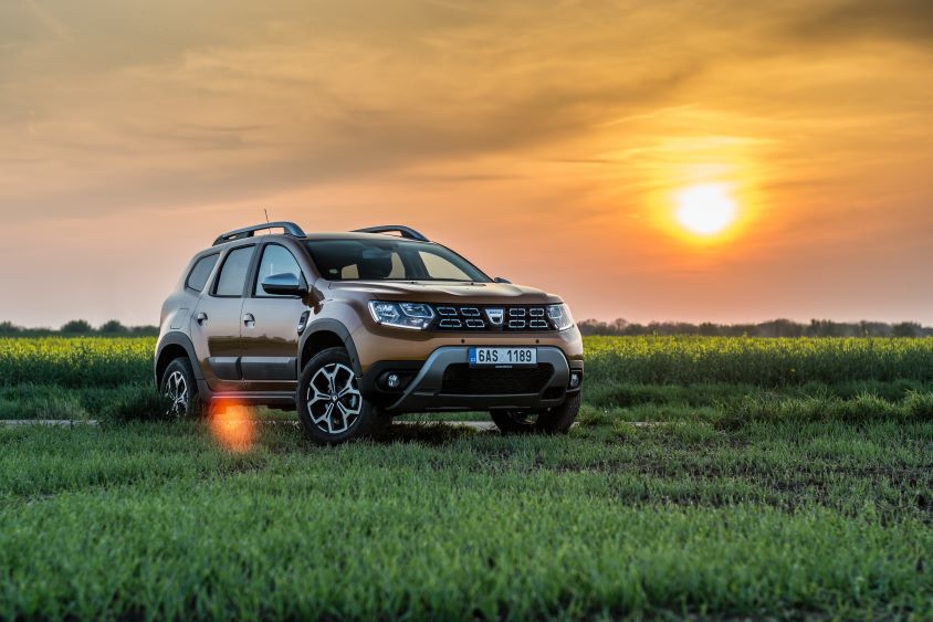 Brown dacia car driving through a field at sunset