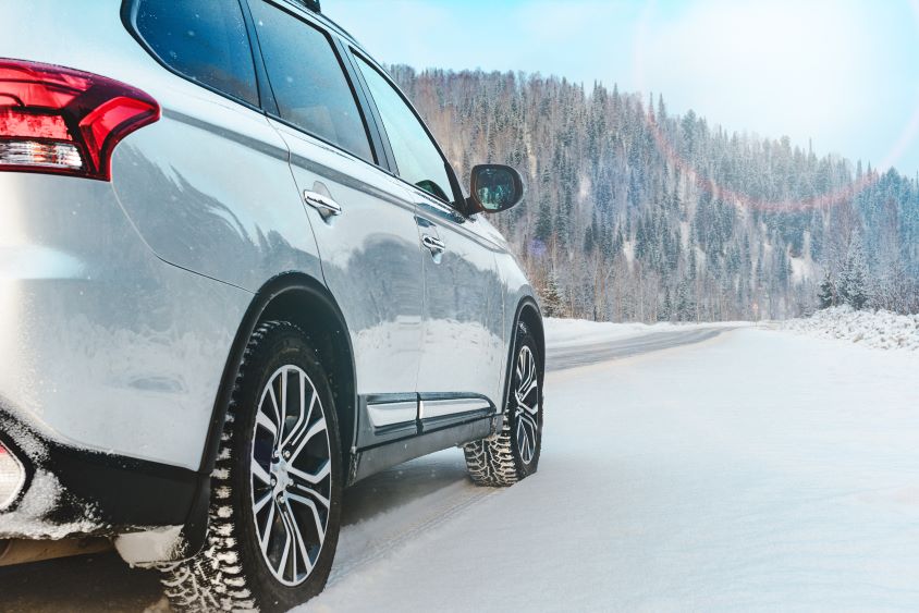 Side of a car driving in snow towards a forest