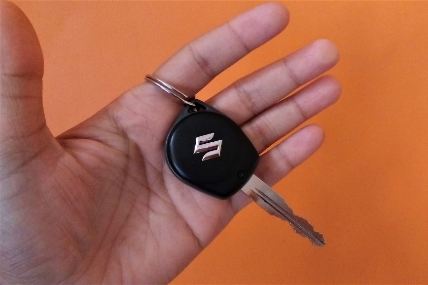 Hand holding car keys with Suzuki logo, orange background