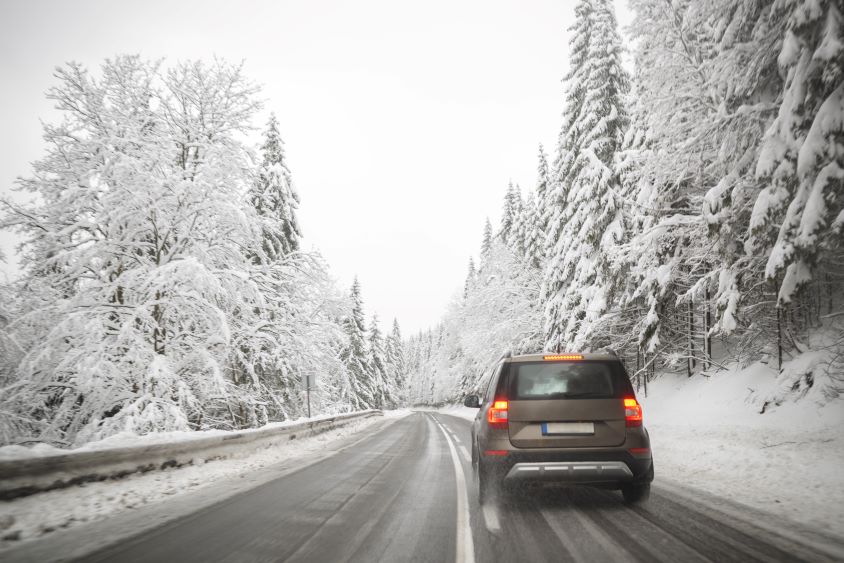 Brown car driving in frosty conditions, trees either side of the road covered in snow