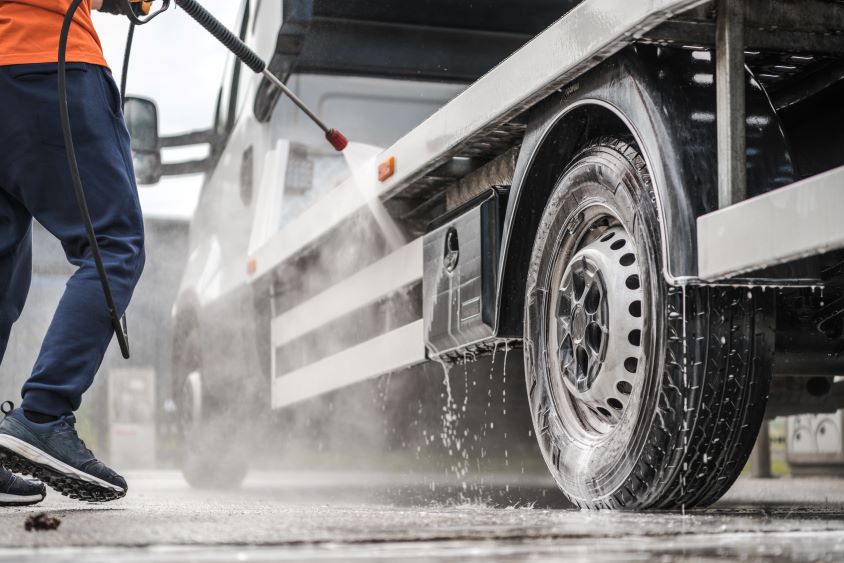 Person with a pressure washer spraying the side of a HGV