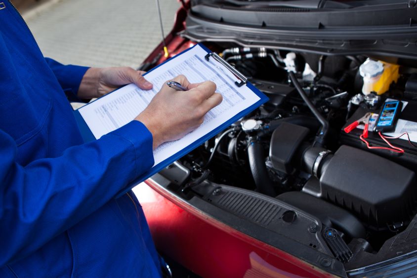 Mechanic with clipboard inspecting a vehicle's engine