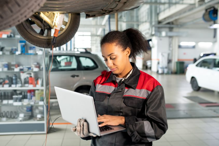 Young female mechanic holding laptop beneath a vehicle