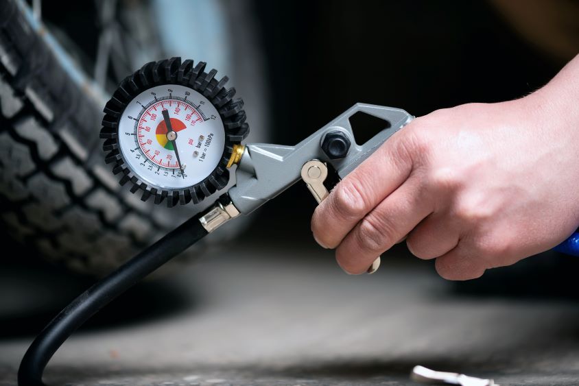 Hand holding pressure gauge next to a car tyre