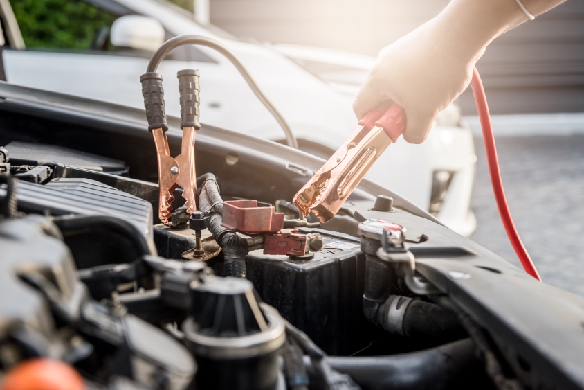 Hand attaching red jump cable to a car engine