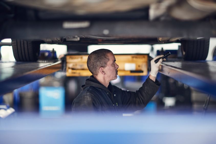 Mechanic working underneath car shining a torch