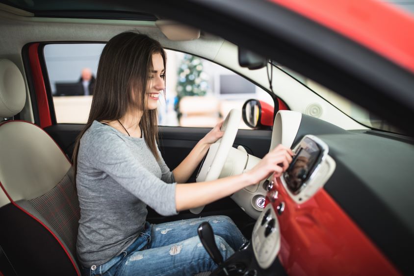 Smiling woman adjusting her car radio in red interior