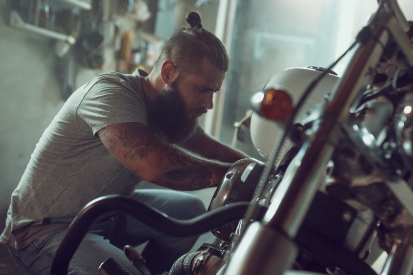 bearded man kneeling next to vehicle, doing repairs