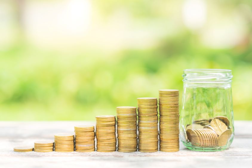 A row of gold coins stacked next to a half full jar of coins with green background