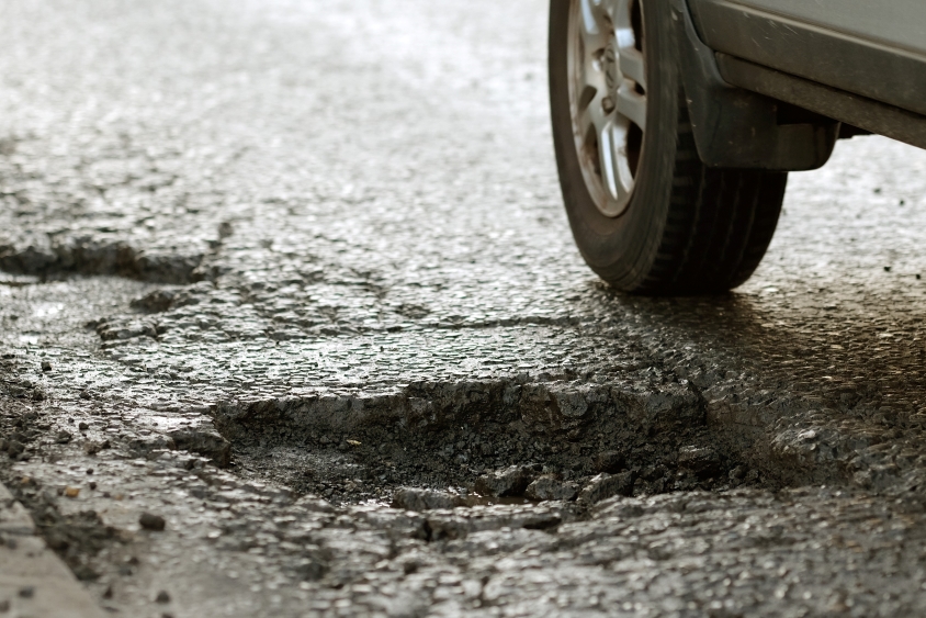 Tire of a car narrowly missing a pothole on road