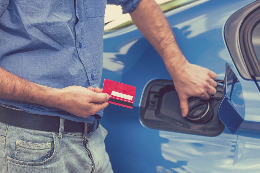 Man opening fuel tank of car while holding a card for payment