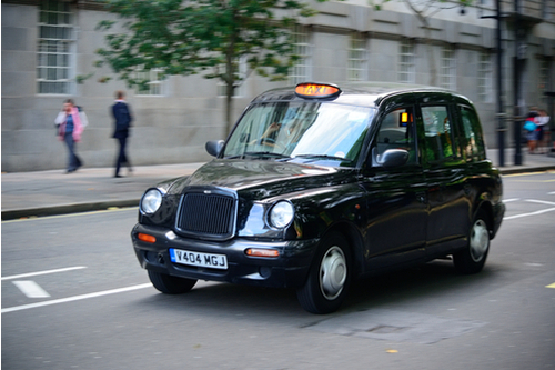 Image of a London black cab pulling up to a pedestrian crossing with traffic lights