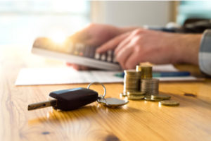 Image of car keys and money on a table with a man using a calculator