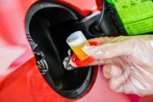 Photo of a gloved hand adding liquid into a car's fuel tank