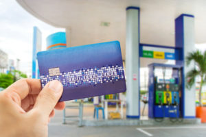 Image of a hand holding a fuel card outside a forecourt with filling pumps in the background