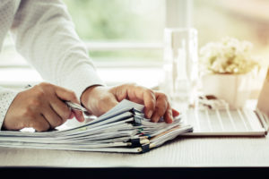 Businessman dealing with pile of paperwork with pen and laptop