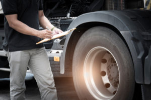 Truck driver holding clipboard daily checking safety truck wheels, vehicle maintenance checklist program.