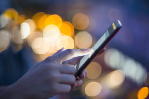 Female using her mobile phone, city skyline night light background