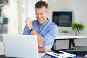 Middle aged businessman wearing shirt while sitting at office desk and using his computer.