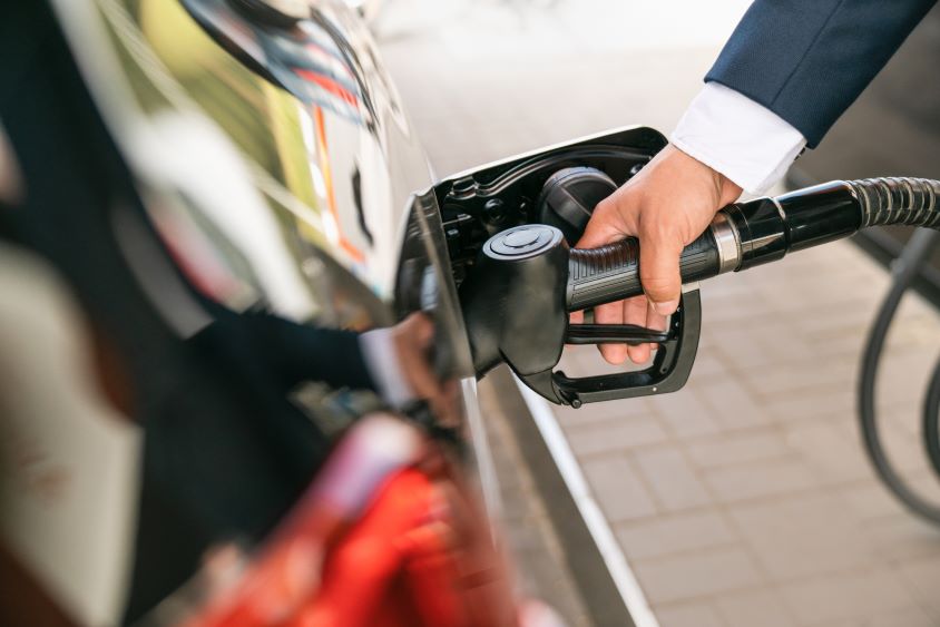 Man's hand inserting fuel nozzle into black car