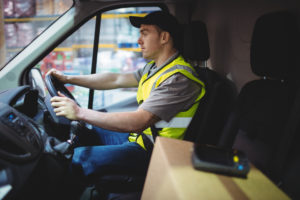 Image of a delivery driver at the wheel of a van, with a parcel in the foreground on a seat