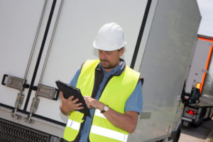 A driver records information on a tablet near an HGV.