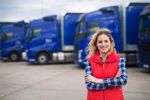 Female truck driver in red gilet standing in front of a row of blue HGVs