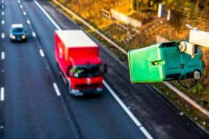 Green average speed camera pointed at red lorry driving on motorway