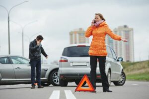 Warning triangle placed on road whilst woman is on the phone after car accident