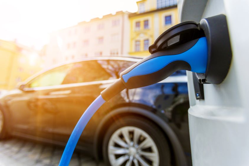 Blue electric car charger in socket with black car in background