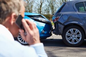 Man holds phone to ear whilst looking at a car accident