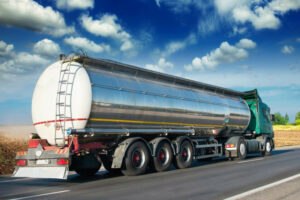 Tanker driving on road next to field, shipping a large tank