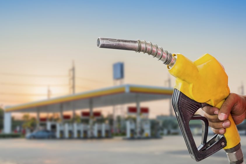 Hand holding yellow fuel nozzle in front of fuelling station