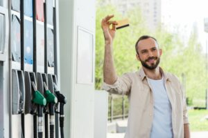 Smiling man holds up fuel card next to fuel pumps