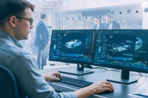 Man sitting at computer with two monitors with car grapbics