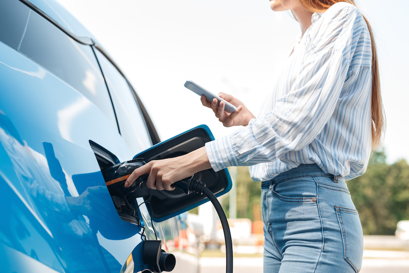 woman charging electric vehicle whilst using phone